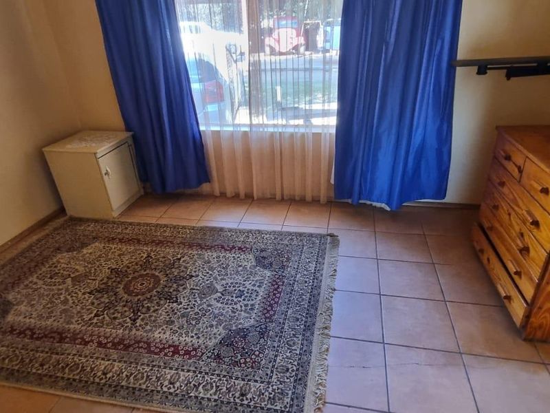 A bedroom featuring tiled flooring, a large window with curtains, and built-in electrical outlets.