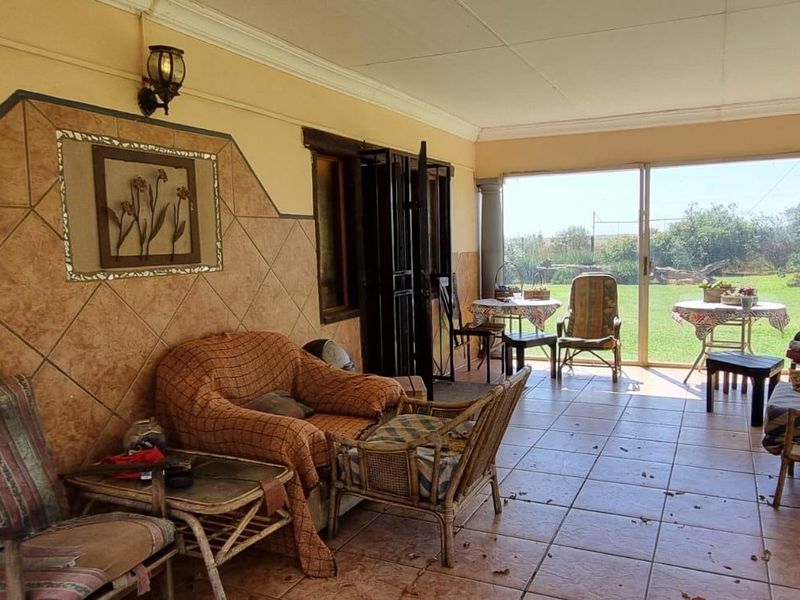 A covered patio area featuring tiled flooring, decorative wall tiling, and sliding glass doors leading out to a spacious garden.