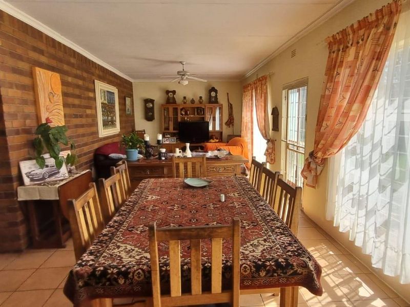 Spacious open-plan living and dining area featuring a prominent face-brick feature wall, tiled flooring, and large windows providing ample natural light.