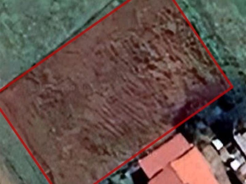 An aerial view of a vacant residential plot of land, clearly outlined in red, showing the site boundaries and surrounding area.