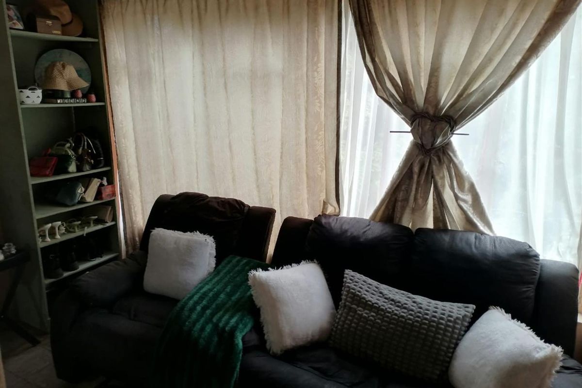A living room area featuring built-in shelving and large windows covered by curtains.