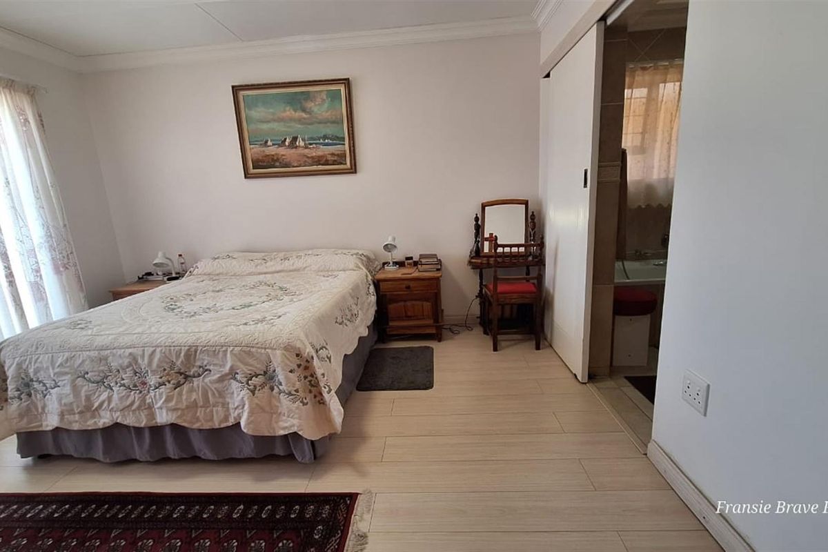 A well-lit bedroom featuring light-toned tiled flooring, crown molding, and an en-suite bathroom access point with a sliding door.