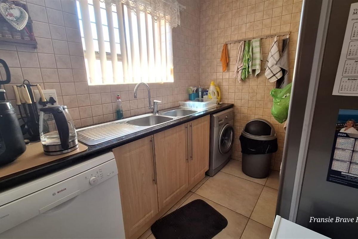 A functional kitchen featuring tiled walls, laminate cabinetry, a double sink, and dedicated space for laundry appliances.