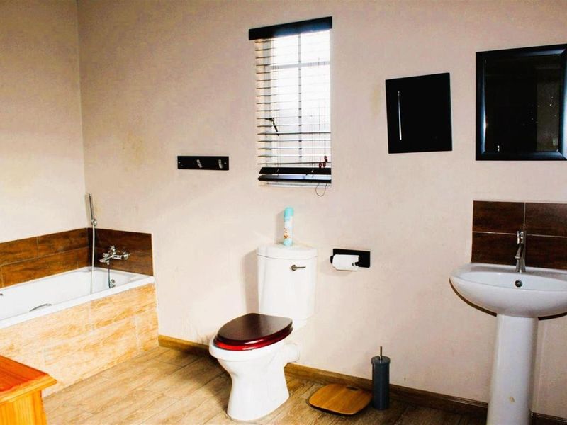 A functional bathroom featuring a built-in bathtub with tiled surround, a pedestal basin, and a standard toilet with wood-finish seat.