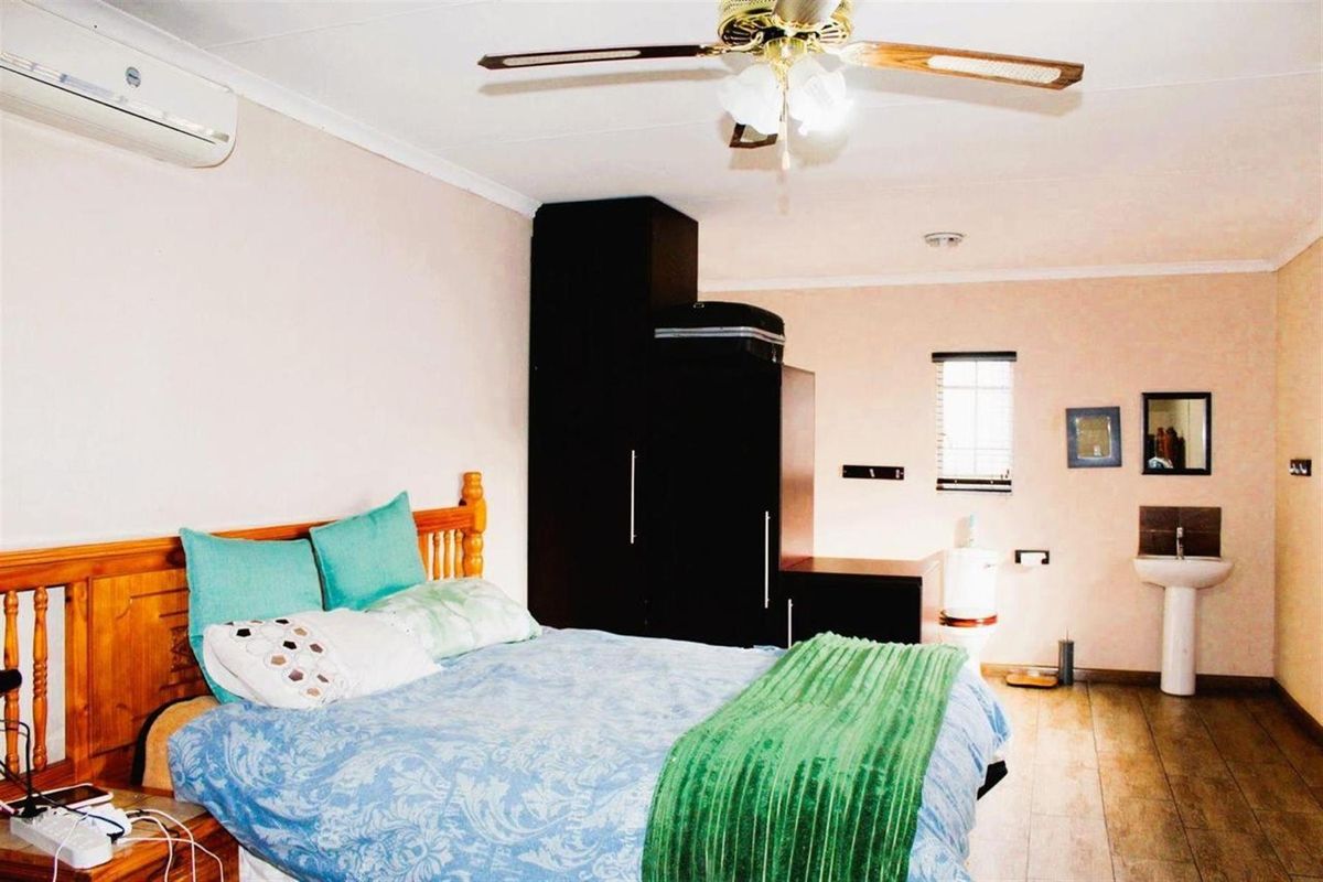 A bedroom featuring wood-look flooring, a ceiling fan, wall-mounted air conditioning unit, and an integrated en-suite bathroom area with a pedestal basin and toilet.