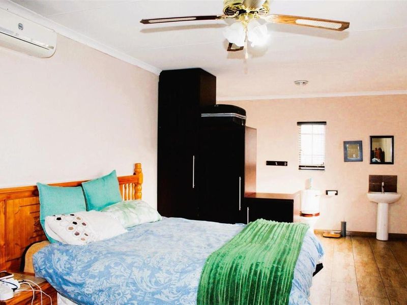 A bedroom featuring wood-look flooring, a ceiling fan, wall-mounted air conditioning unit, and an integrated en-suite bathroom area with a pedestal basin and toilet.