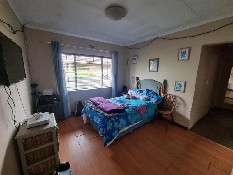 A functional bedroom featuring timber flooring, a large window with security bars, and a central ceiling light fixture.