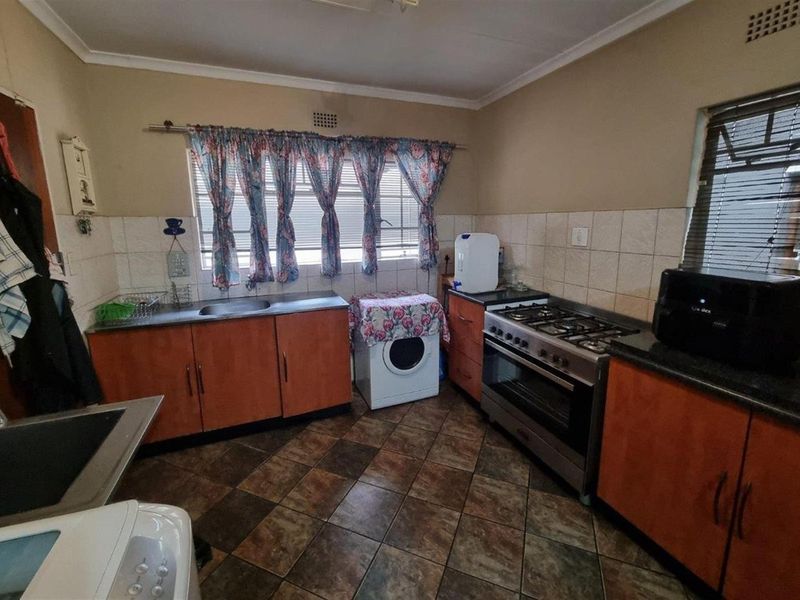 Functional kitchen featuring wooden cabinetry, tiled splashbacks, a gas stove, and tiled flooring with integrated laundry appliance space.