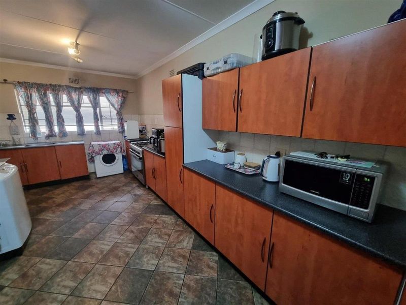 A functional kitchen featuring wood-look cabinetry, dark laminate countertops, tiled flooring, and a built-in stove with extractor fan.