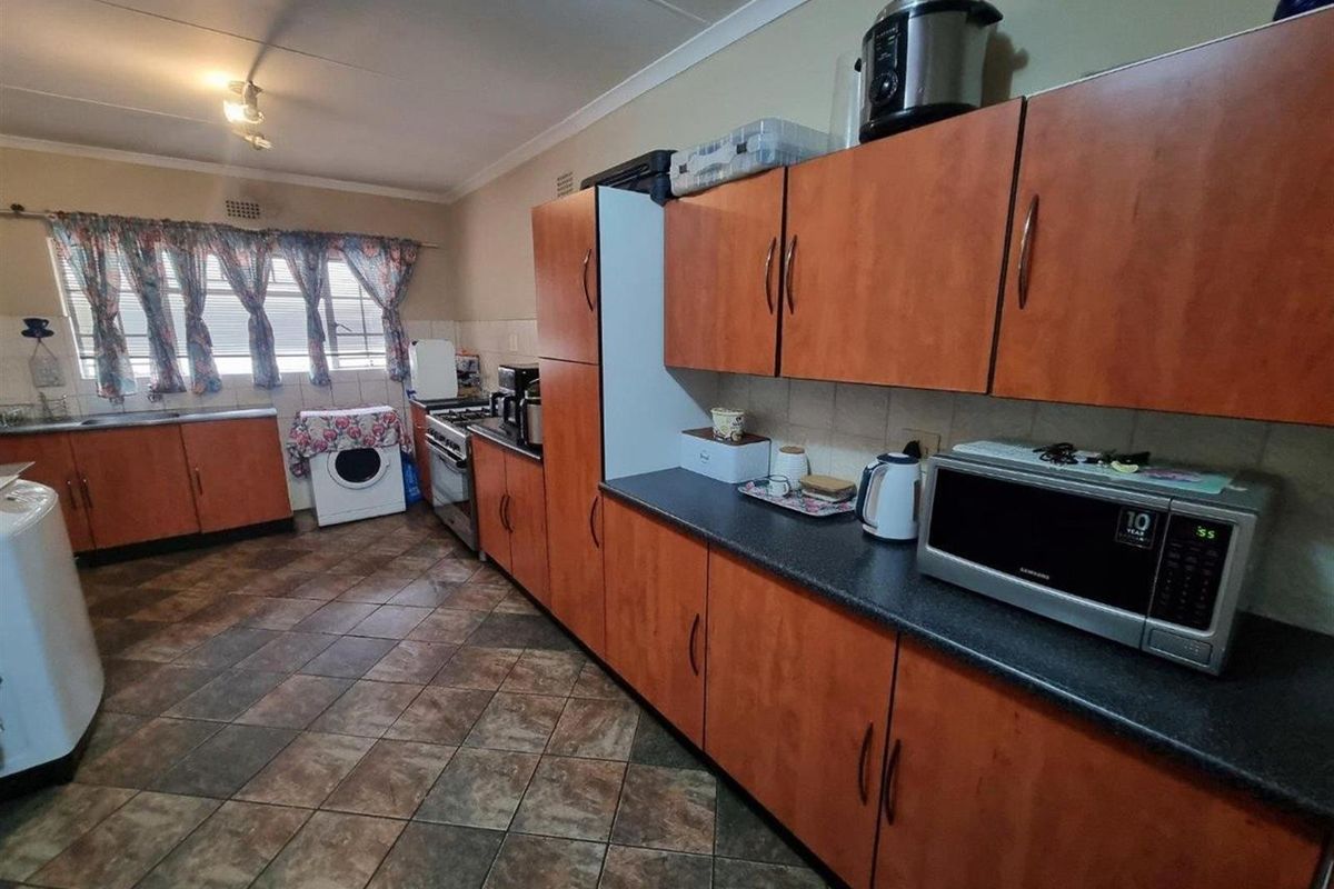 A functional kitchen featuring wood-look cabinetry, dark laminate countertops, tiled flooring, and a built-in stove with extractor fan.