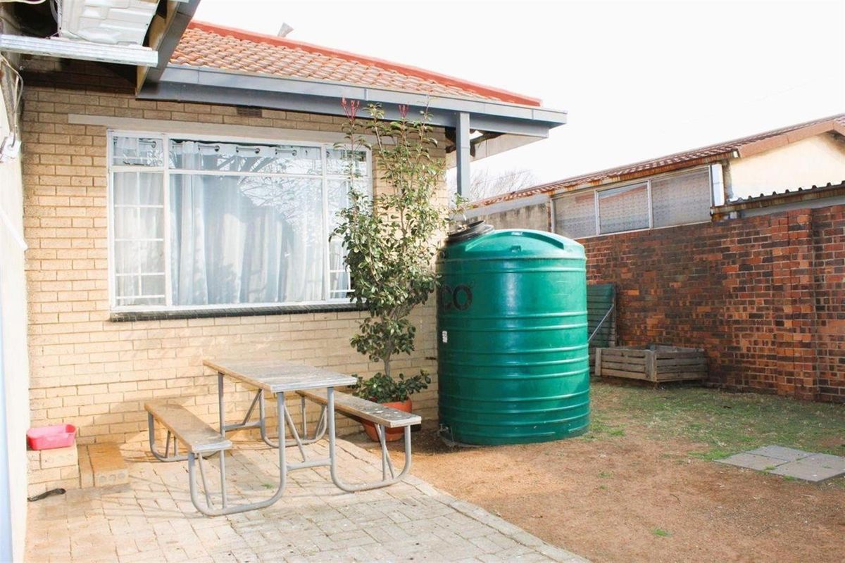 Rear exterior view of the property featuring a paved patio area, brick facade, and a large water storage tank.