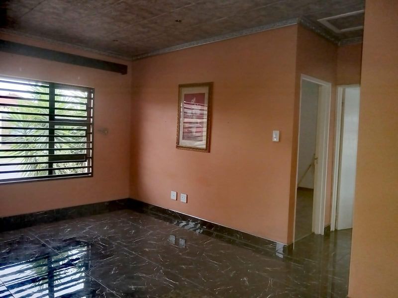 An empty living room featuring dark marble-effect tiled flooring, peach-toned walls, and security bars on the window.