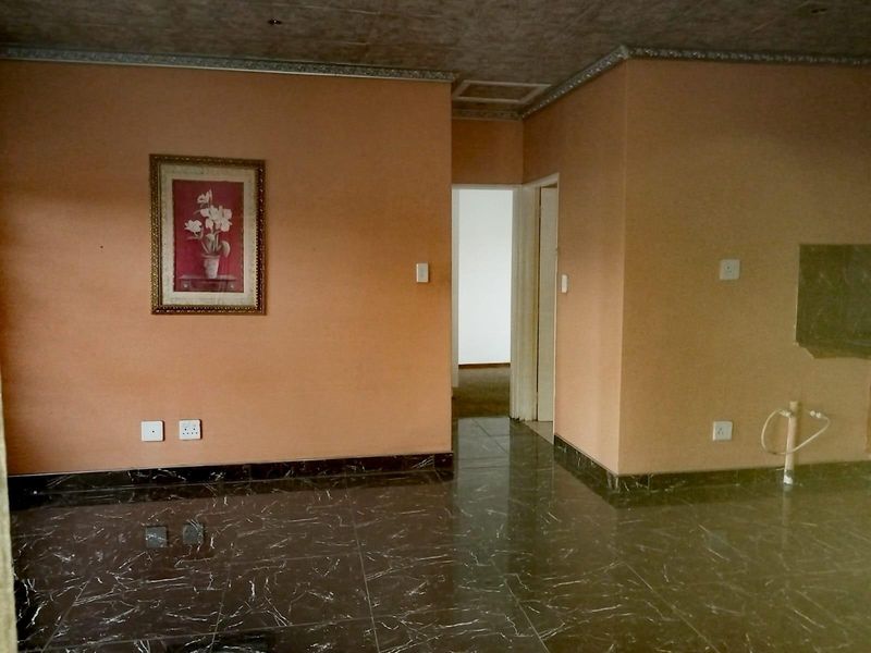 An empty living area featuring dark marble-look floor tiles, decorative ceiling cornices, and peach-toned walls with visible electrical and plumbing points.