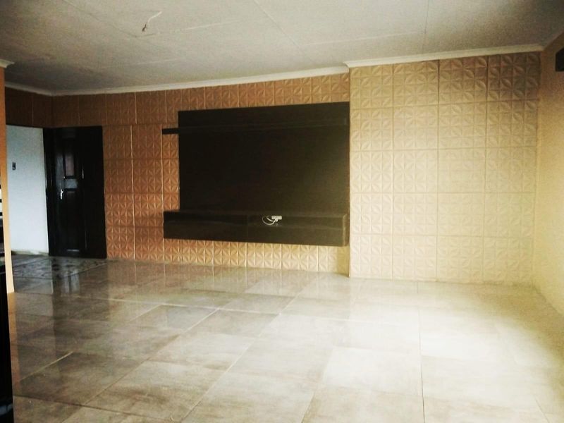 Spacious living area featuring large-format floor tiles, a built-in media console, and decorative textured wall paneling.