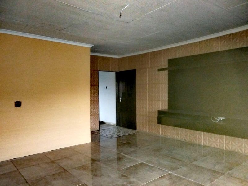 An empty living room featuring large floor tiles, textured wall tiling, and a built-in wall unit, requiring minor electrical finishing.