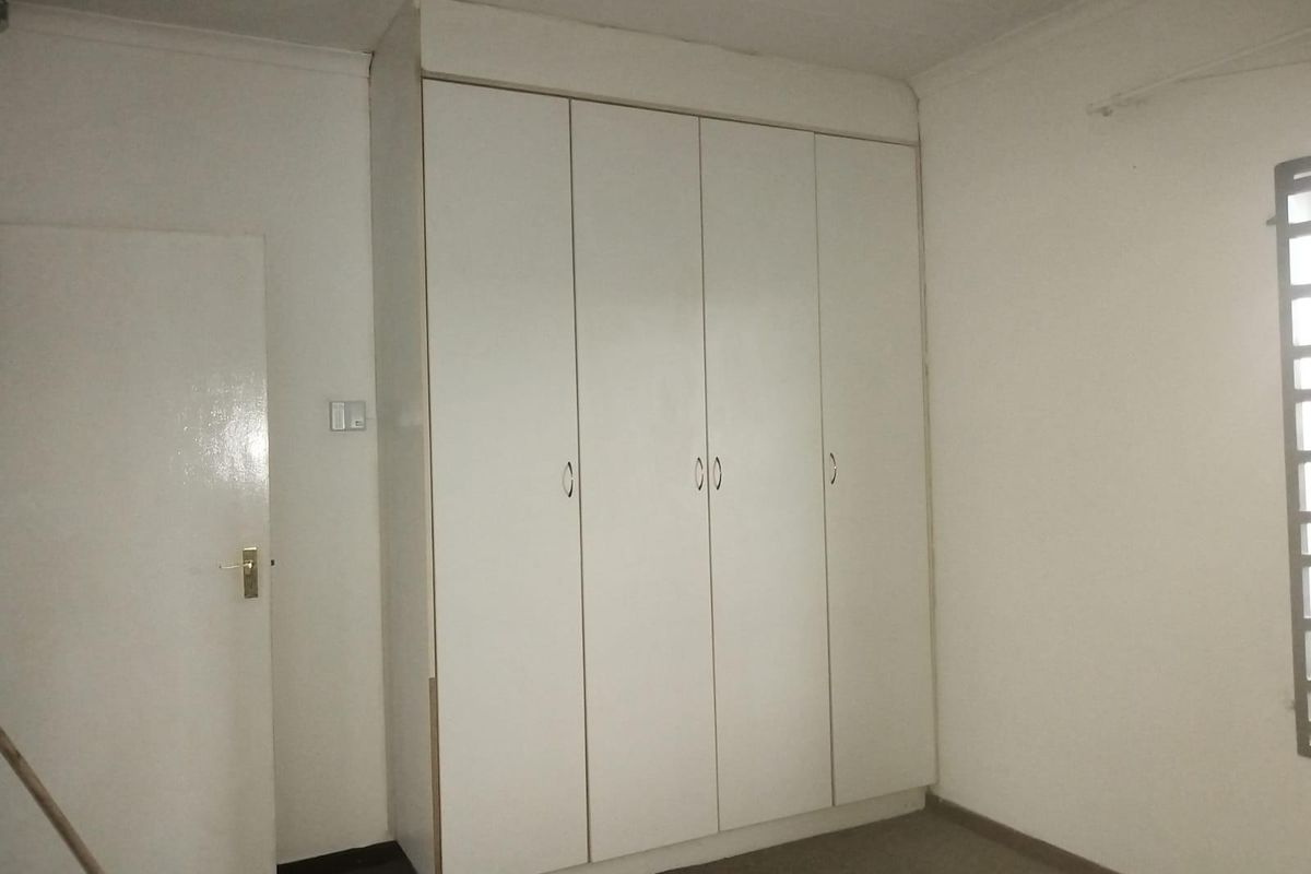 A simple bedroom featuring built-in cupboards, neutral walls, and carpeted flooring, offering a blank canvas for potential interior design updates.