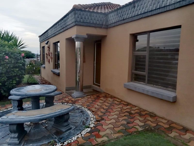 A side view of the house featuring a paved patio area, decorative column, and tiled roof with detailed trim.