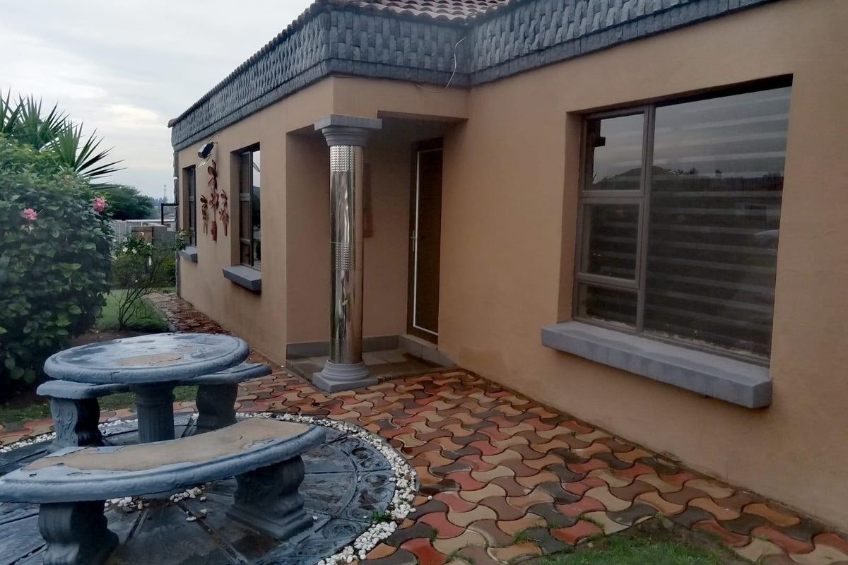 A side view of the house featuring a paved patio area, decorative column, and tiled roof with detailed trim.