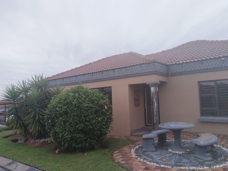 Front elevation of a single-story house featuring a tiled roof, decorative trim, aluminium window frames, and a paved outdoor seating area.