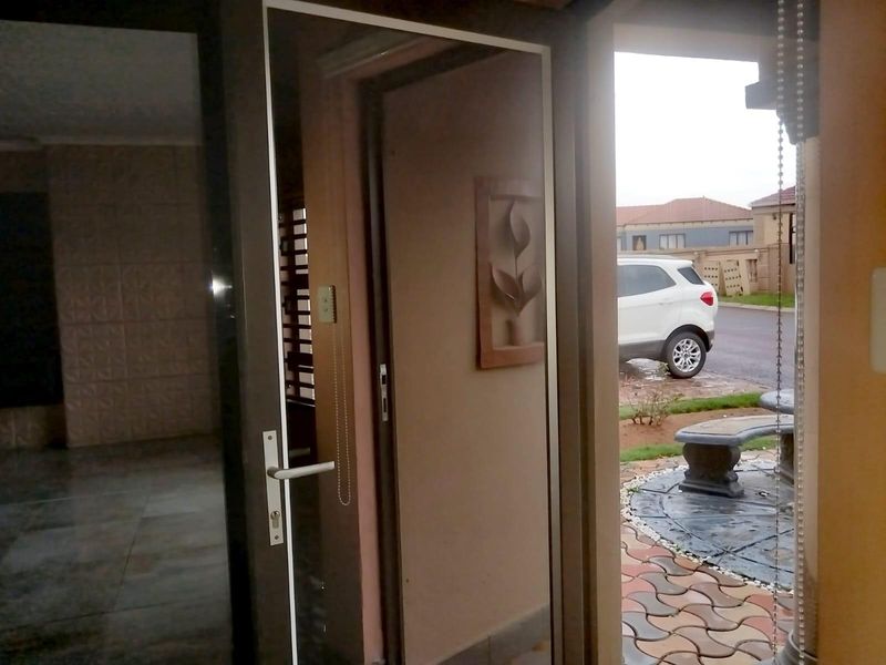 View from the interior looking out through a glass entrance door towards the paved front garden and driveway.