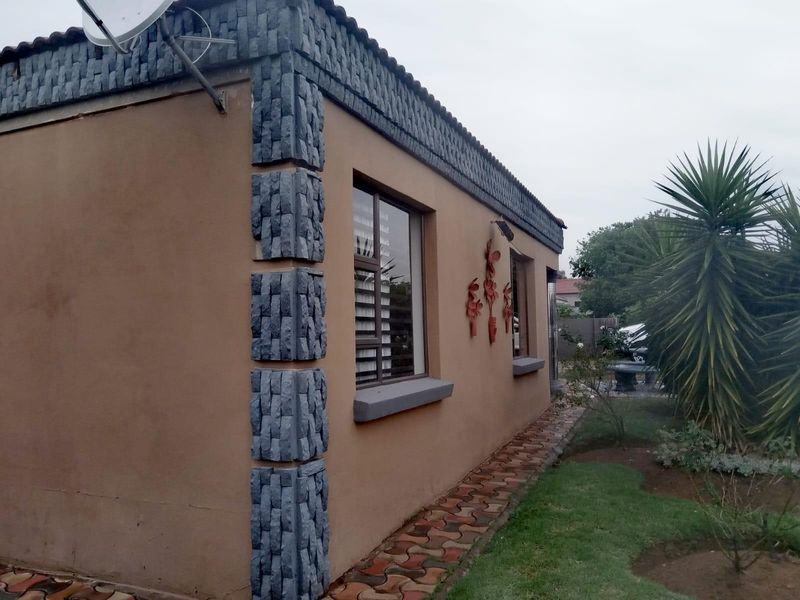 Side view of the property featuring stone cladding corner accents, aluminium window frames, and a paved walkway leading through the garden.