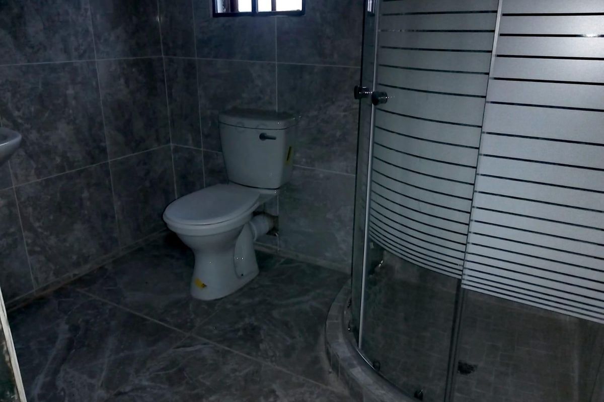 A functional bathroom featuring a toilet and a curved glass shower enclosure with grey marble-effect wall and floor tiling.