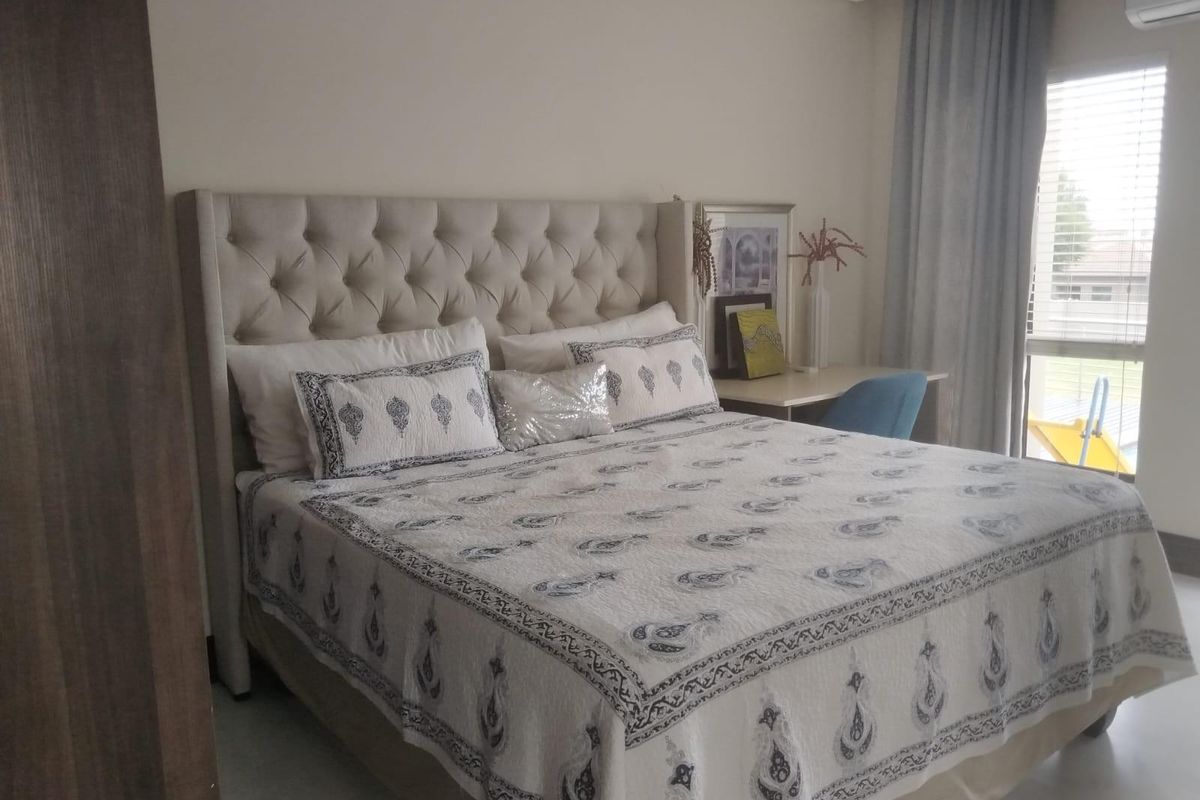 A well-maintained bedroom featuring neutral wall tones, tiled flooring, a built-in wardrobe, and a window with fitted blinds and curtains.