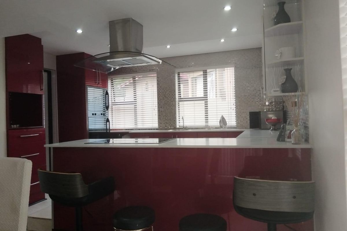 Modern kitchen featuring high-gloss red cabinetry, a central island with a built-in hob, stainless steel extractor fan, and mosaic tile backsplash.