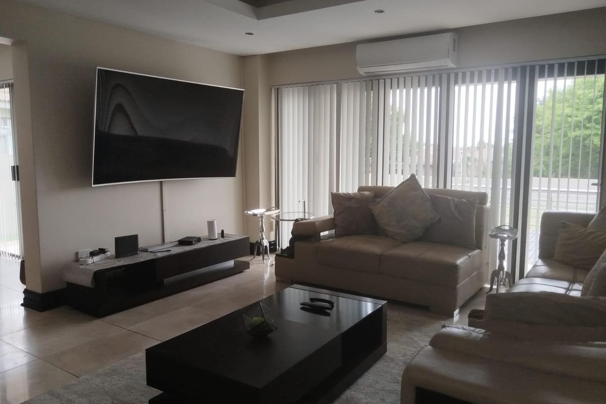 A spacious living room featuring tiled flooring, recessed ceiling lighting, and a wall-mounted air conditioning unit with large sliding glass doors.