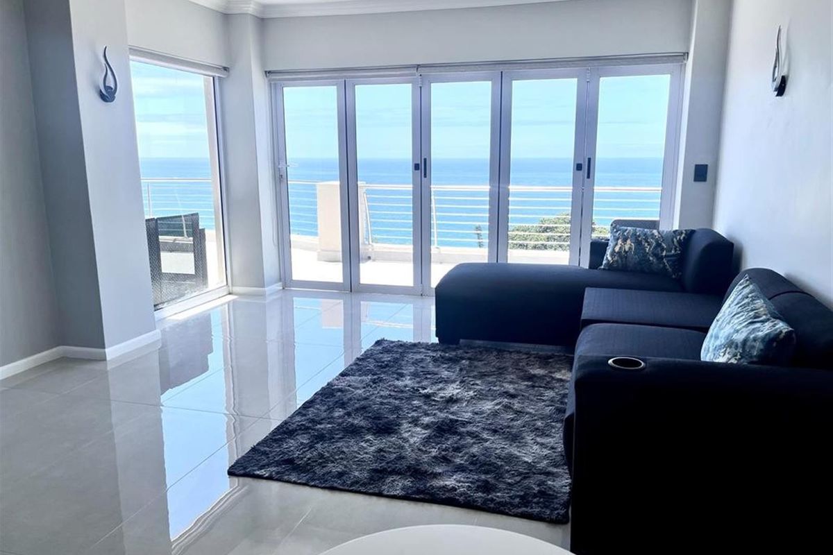 Bright living room featuring large glass folding doors that open to a balcony with expansive ocean views and polished tile flooring.