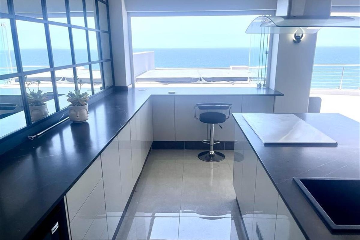 Modern kitchen featuring sleek cabinetry, dark stone countertops, a central island, and expansive ocean views through large windows.