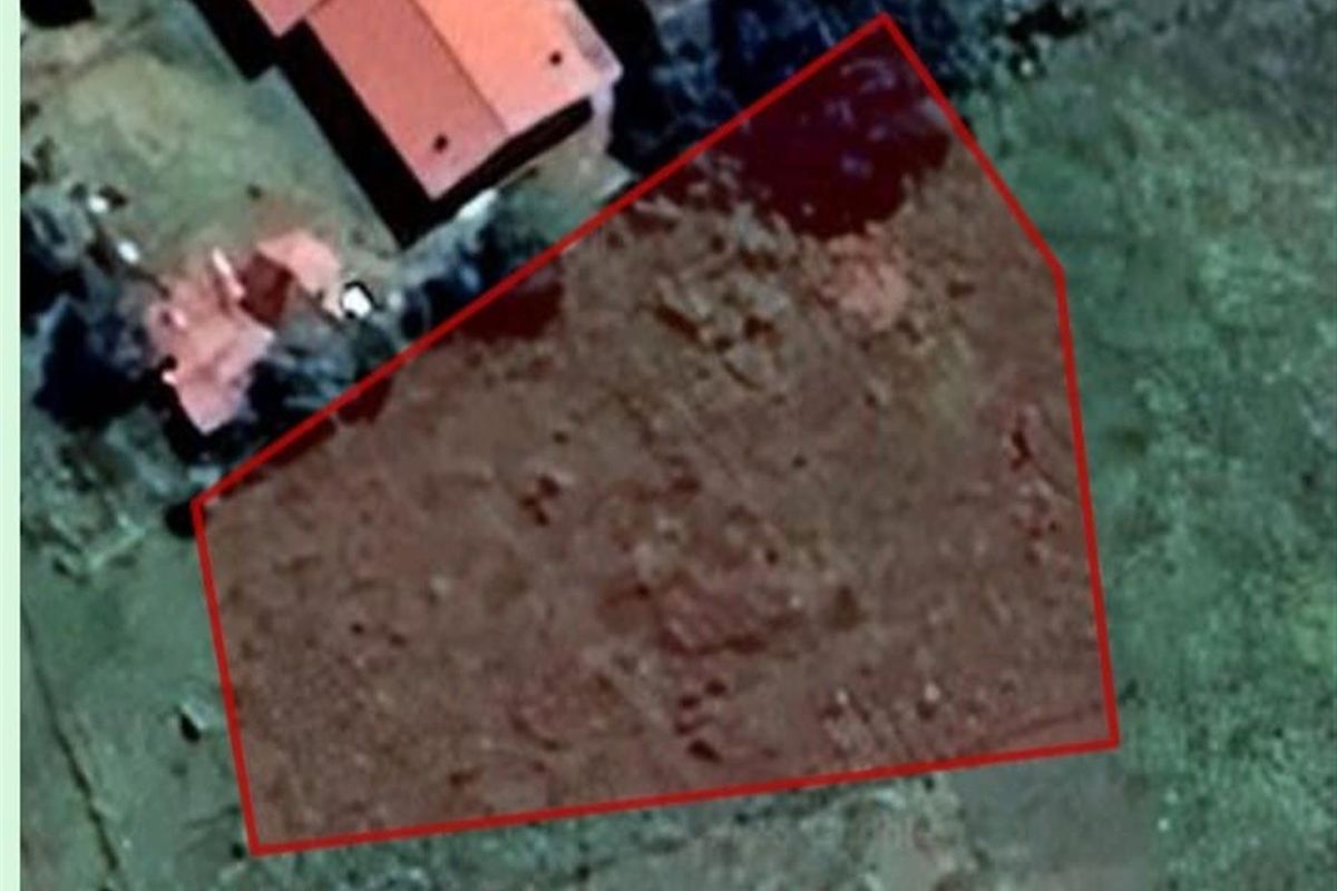 An aerial view of a vacant residential plot with a red boundary overlay indicating the property lines.