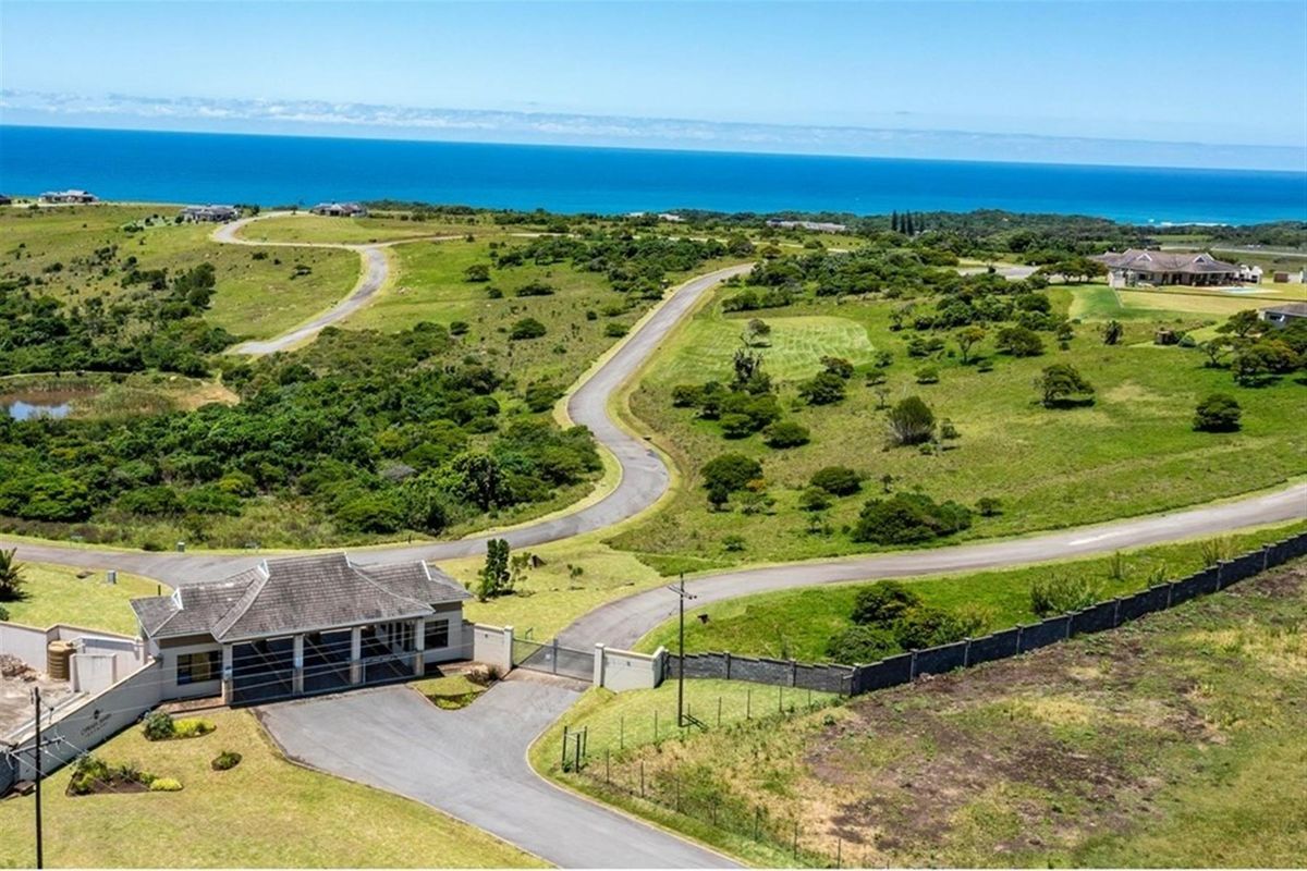 Aerial view of a residential estate entrance featuring paved access roads, security gatehouse, and expansive coastal landscape views.