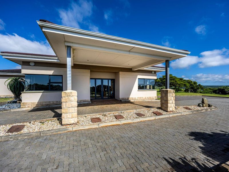 A well-maintained residential property entrance featuring a covered portico, stone-clad pillars, and a paved driveway.