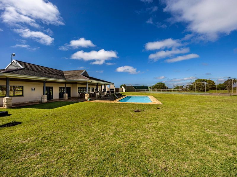 Rear view of the property featuring a spacious lawn, swimming pool, covered patio, and a fenced tennis court in the background.