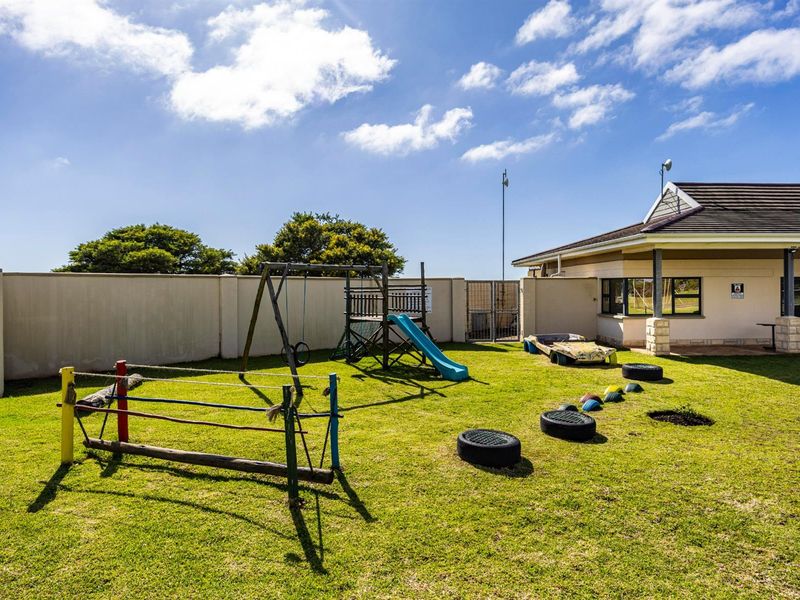 A well-maintained outdoor play area featuring a lawn, perimeter boundary wall, and fixed playground equipment adjacent to the main building structure.