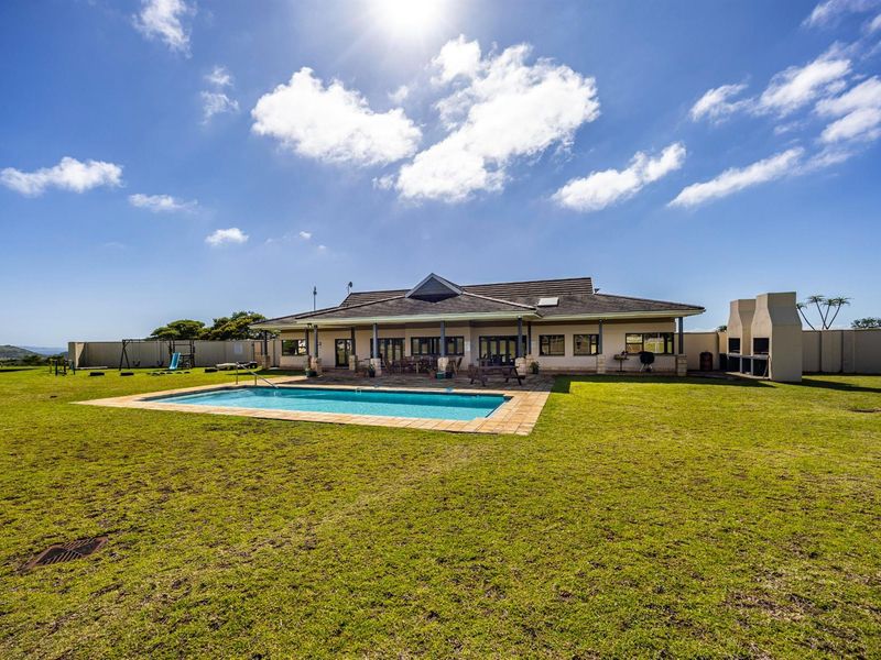 Spacious rear exterior view featuring a well-maintained swimming pool, expansive lawn, and a covered patio area with a built-in outdoor fireplace.