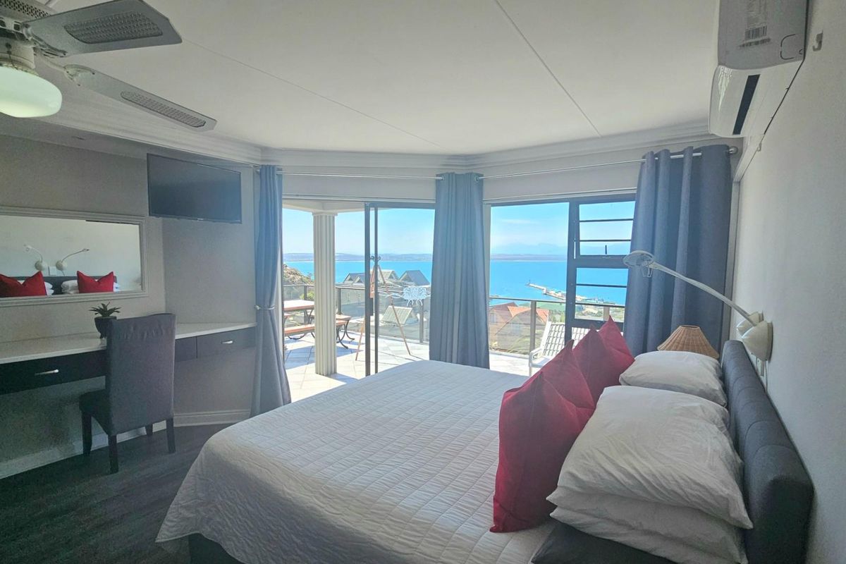 Spacious bedroom featuring a built-in desk, ceiling fan, wall-mounted air conditioning unit, and sliding glass doors opening to a balcony with scenic ocean views.
