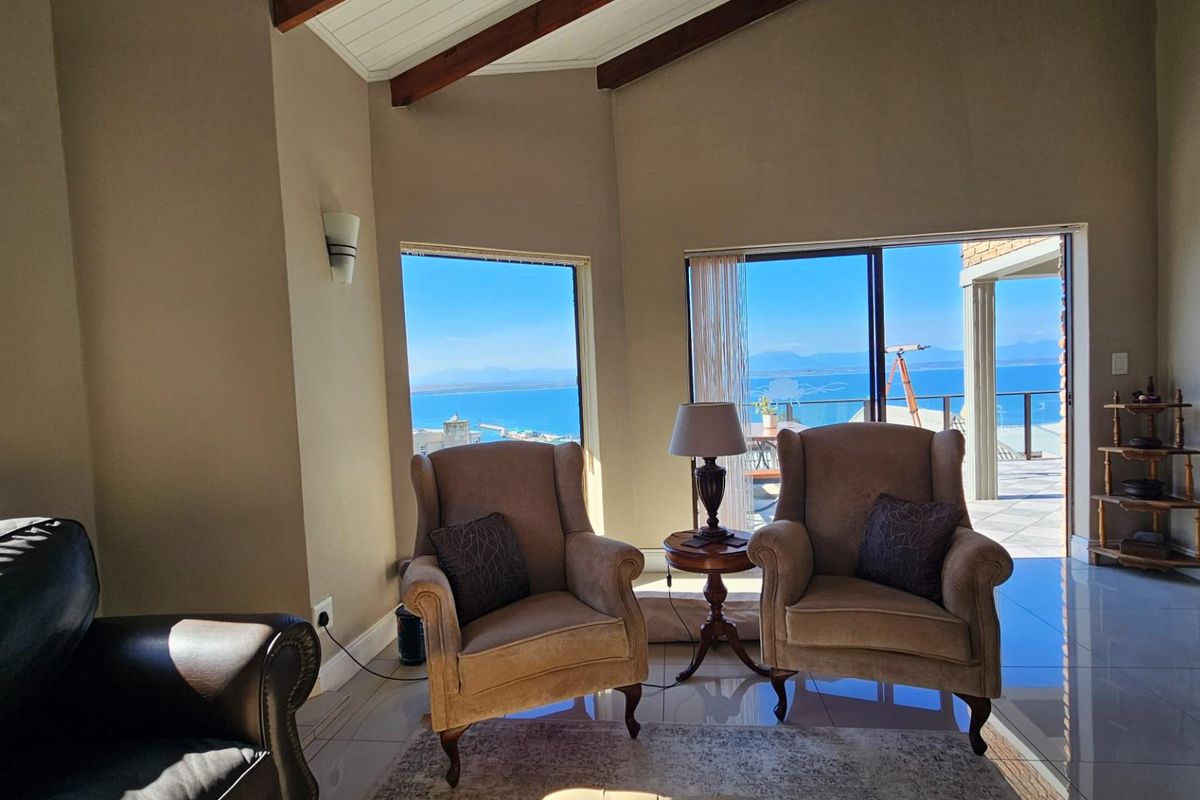 Spacious living area featuring vaulted ceilings with exposed timber beams, large windows, and sliding glass doors opening to a scenic balcony with ocean views.