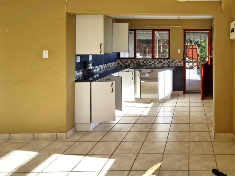 A functional kitchen area featuring tiled flooring, built-in cabinetry, and a tiled backsplash, with direct access to an outdoor area through a security gate.