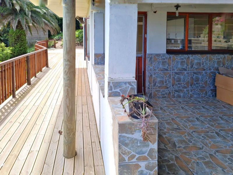 A covered patio area featuring stone-clad walls, tiled flooring, and an adjacent wooden deck with a timber balustrade.