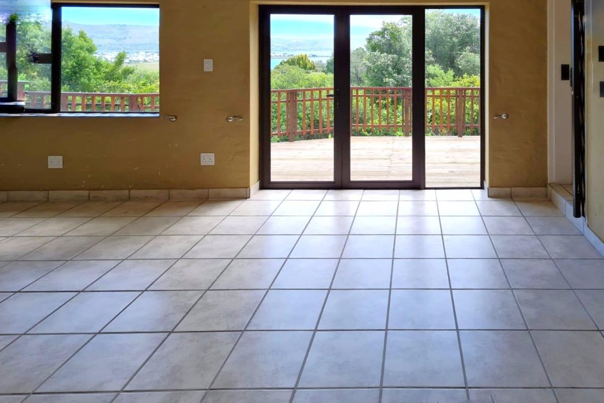 An empty living room featuring tiled flooring, large windows, and double doors leading to an outdoor deck with scenic views.