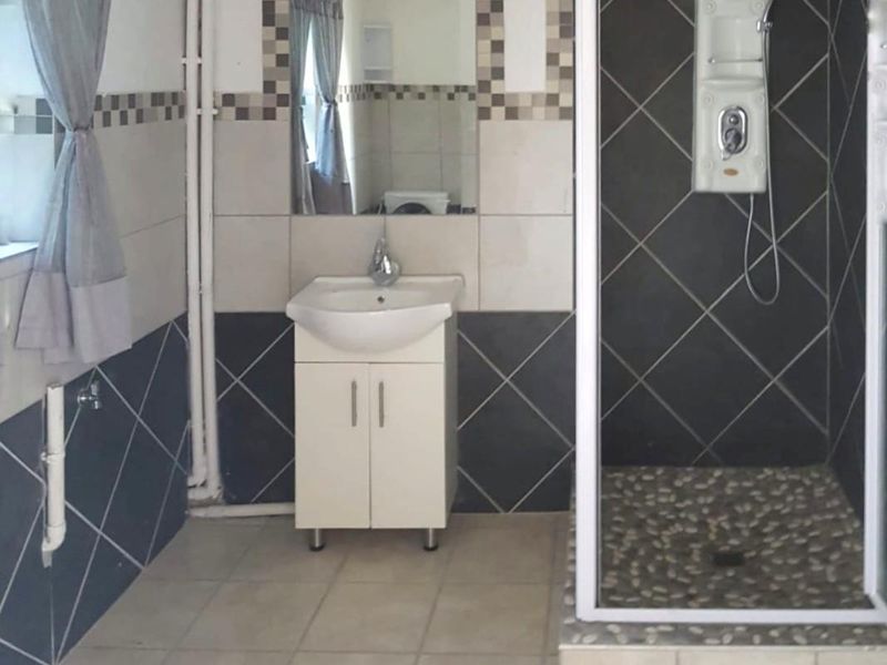 A functional bathroom featuring a shower enclosure, vanity basin, and tiled finishes. The space includes visible surface-mounted plumbing.