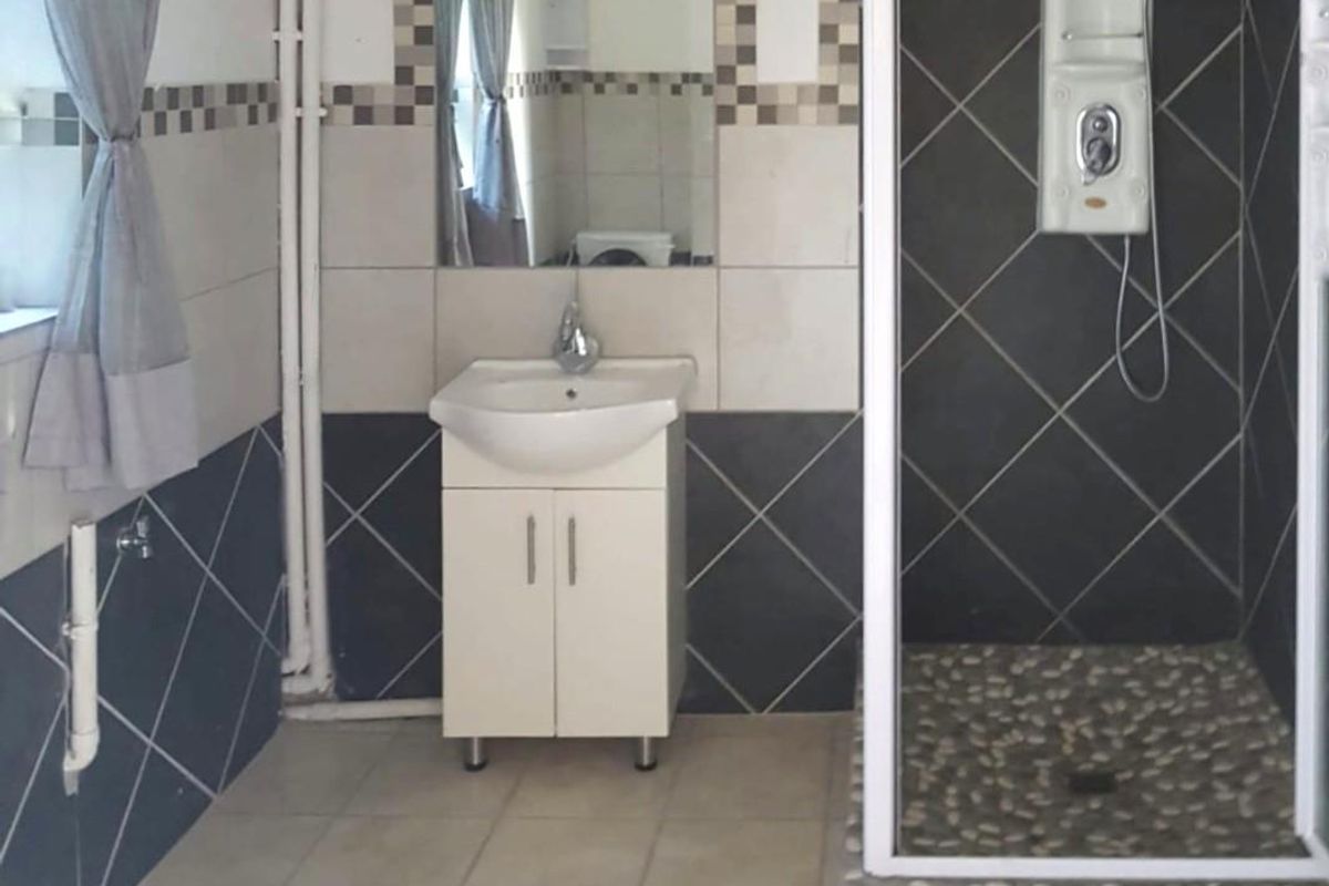 A functional bathroom featuring a shower enclosure, vanity basin, and tiled finishes. The space includes visible surface-mounted plumbing.