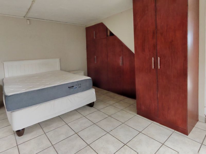 Bedroom featuring tiled flooring and extensive built-in wooden cupboards, with direct access to an adjacent living area.