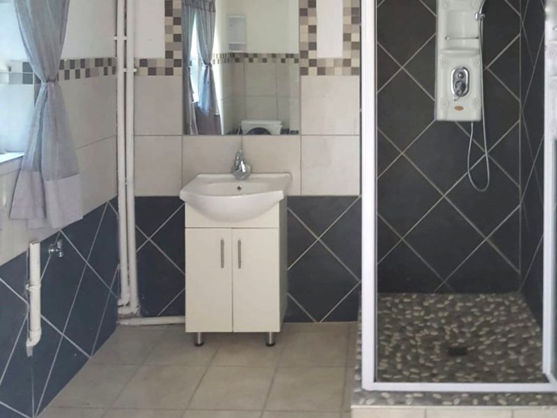 A functional bathroom featuring a shower enclosure with a pebble-style floor, a vanity basin, and visible surface-mounted plumbing pipes.
