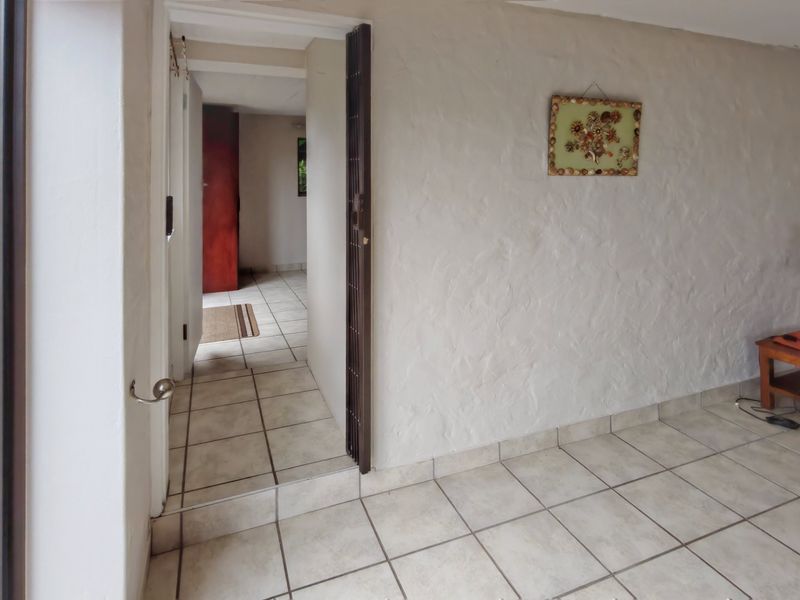 A living area featuring ceramic floor tiles and textured walls, with a security gate leading to an internal hallway.