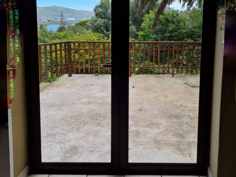A view from the interior through double glass doors onto an outdoor patio featuring a wooden balustrade and scenic landscape views.