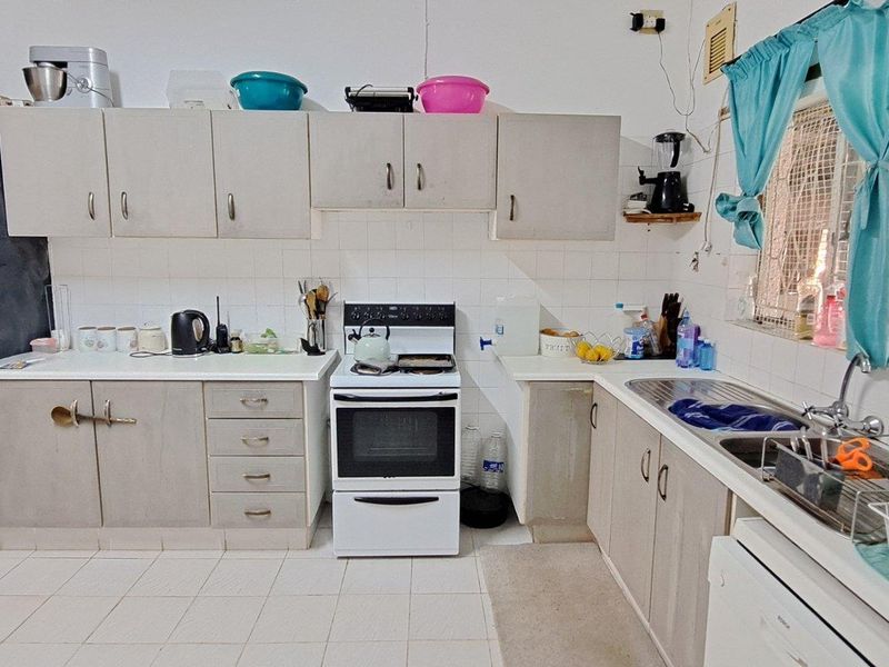 Functional kitchen featuring built-in cabinetry, a freestanding stove, and a stainless steel sink with tiled splashbacks and tiled flooring.