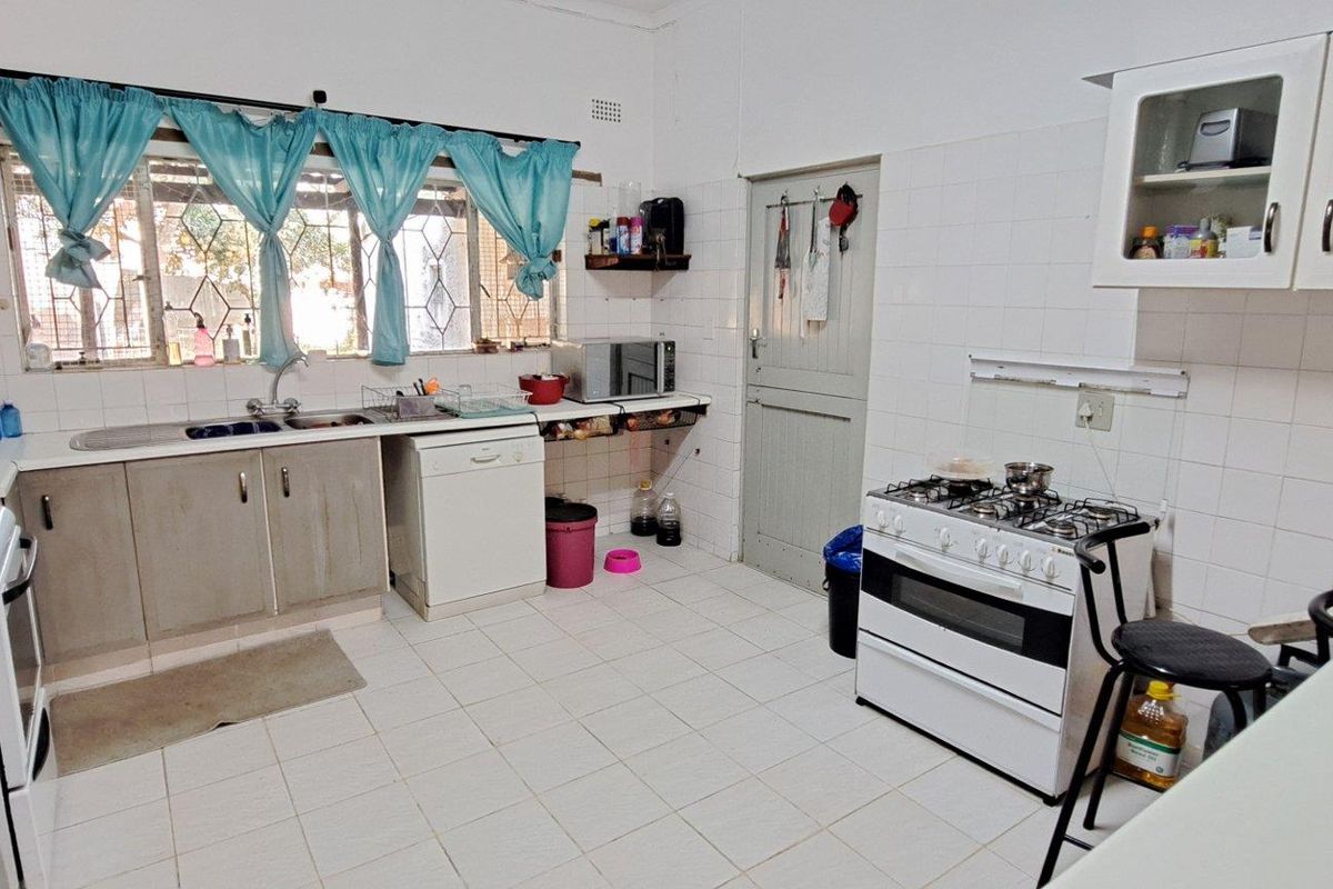 A functional kitchen featuring tiled flooring, white wall tiles, built-in cabinetry, a gas stove, and a double sink with a window view.